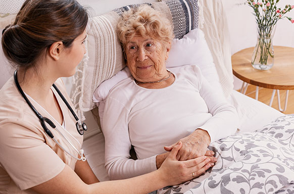 A caregiver accompanying an elderly woman at her bedroom.